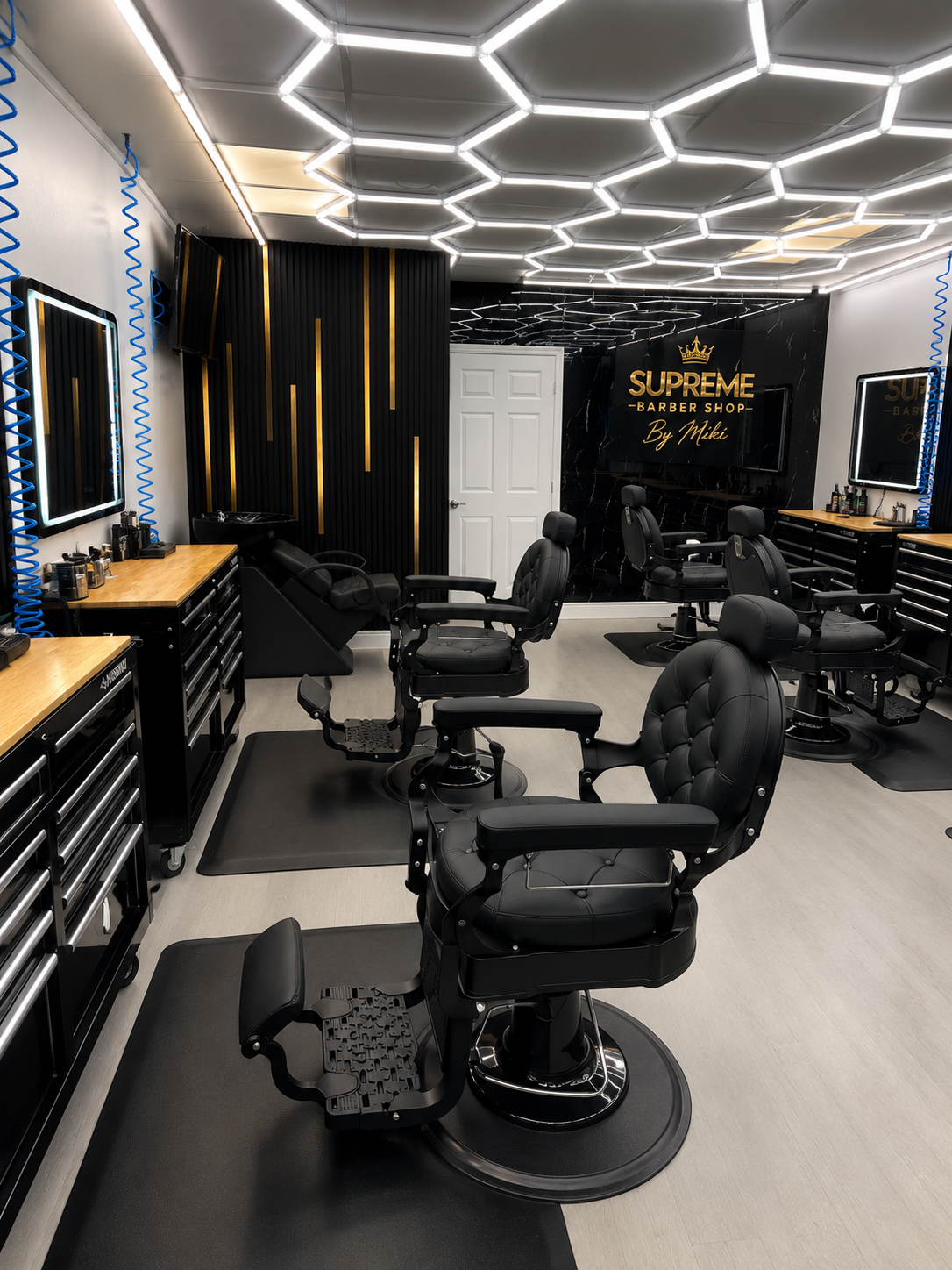 Interior of Supreme Barbershop by Mikki, black marble walls with a gold crown sign, hexagon LED ceiling and black barber chairs